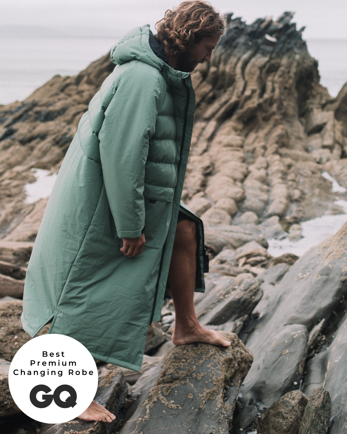 Lead_men - Man wearing a Vivida Lifestyle All Weather Puffer Changing Robe, Aventurine Green Drying Robe for swimming standing on a rock. Sticker: Best Premium Changing Robe - The Independent.