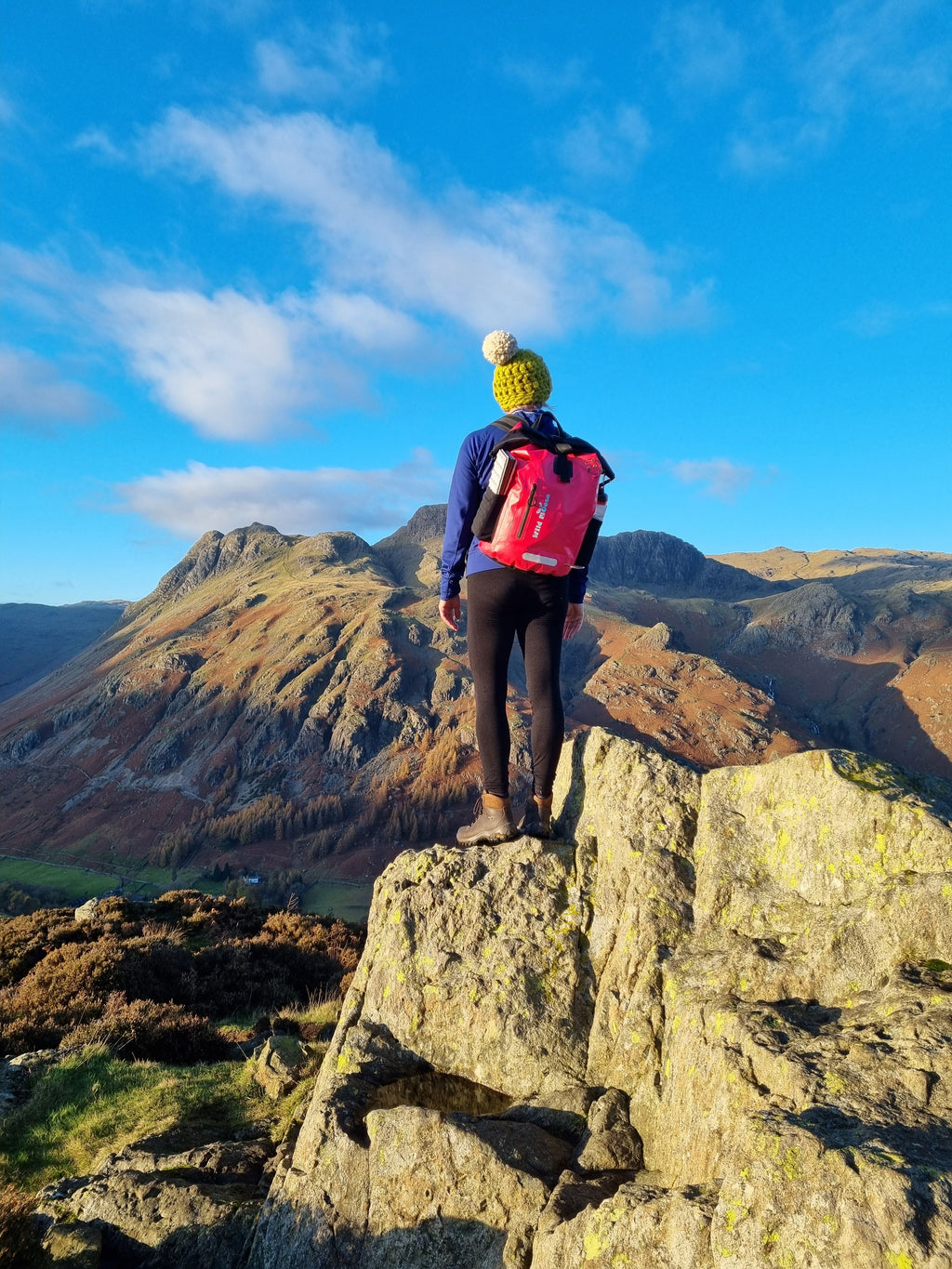 Mountain Climber Hiker wearing bright pink waterproof backpack by Wild Moose, on top of a mountain.
