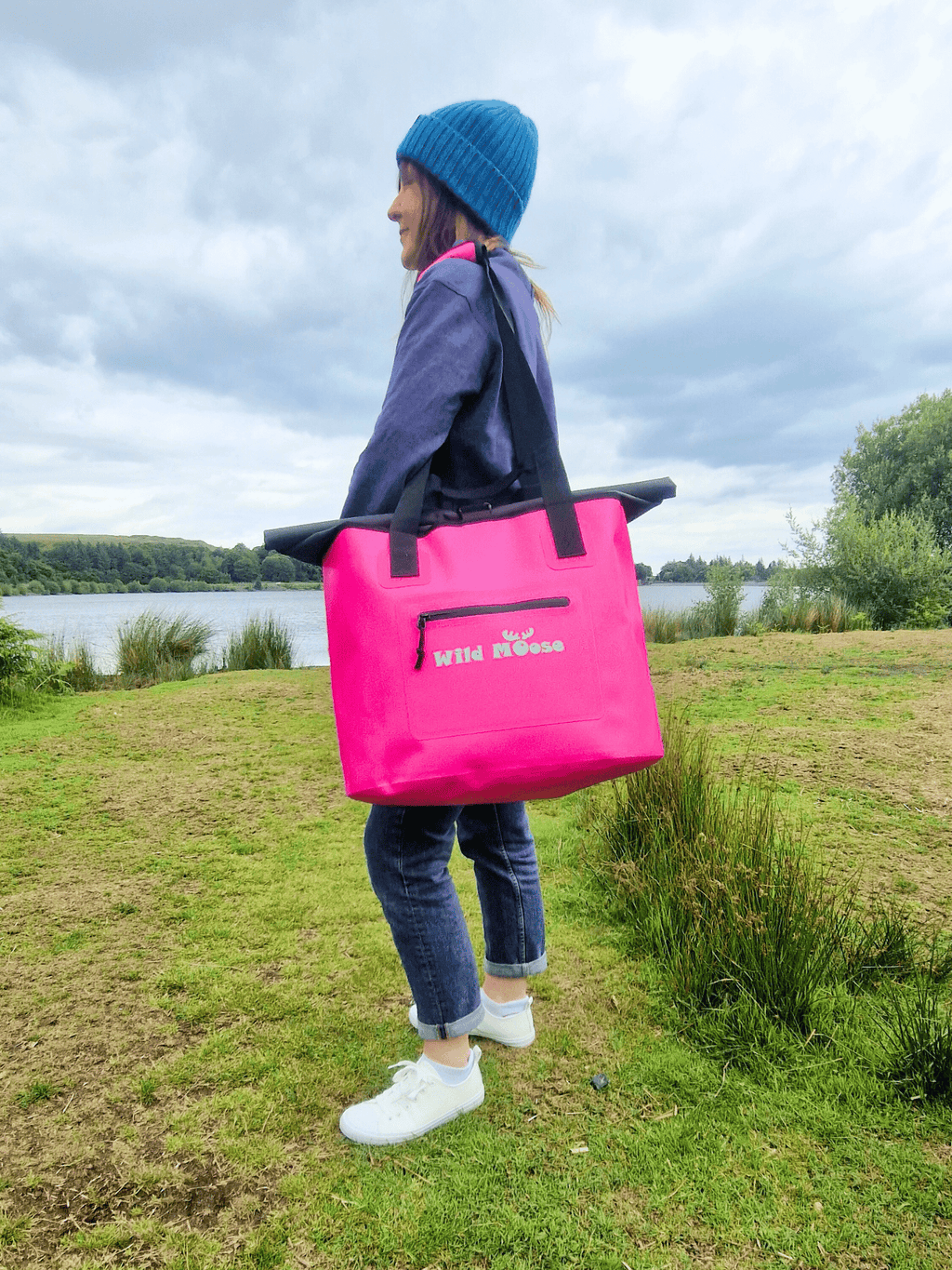 A Wild Swimming Woman Standing with a Bright Pink Wild Moose Waterproof Swim Bag ideal for Outdoor Swimming Kit.