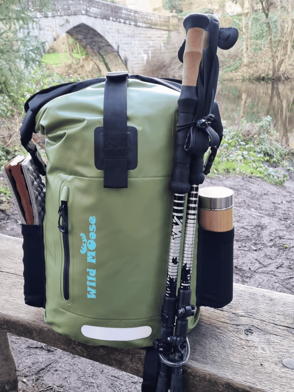 Green waterproof swim backpack by Wild Moose, placed on bench beside swimming river spot
