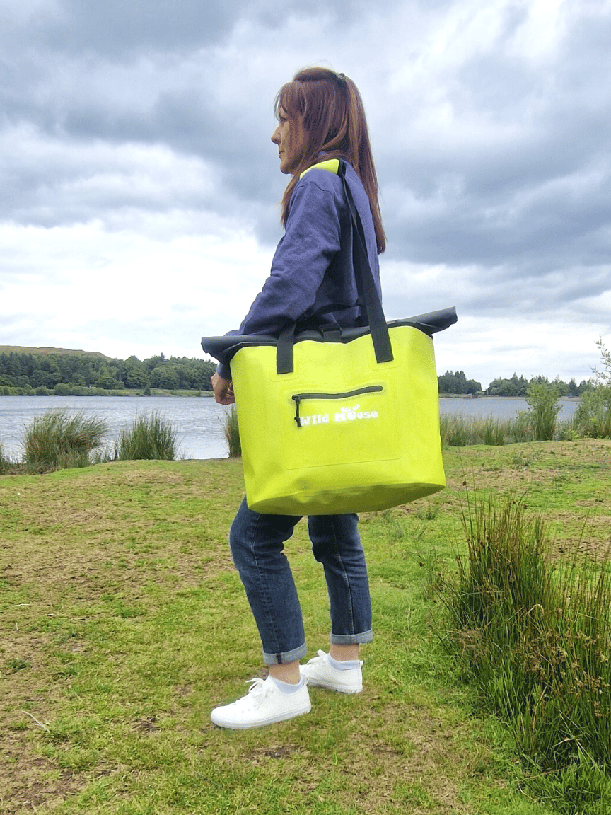 Woman holding Wild Moose yellow waterproof swim bag near lake, ideal for wild swimming kit
