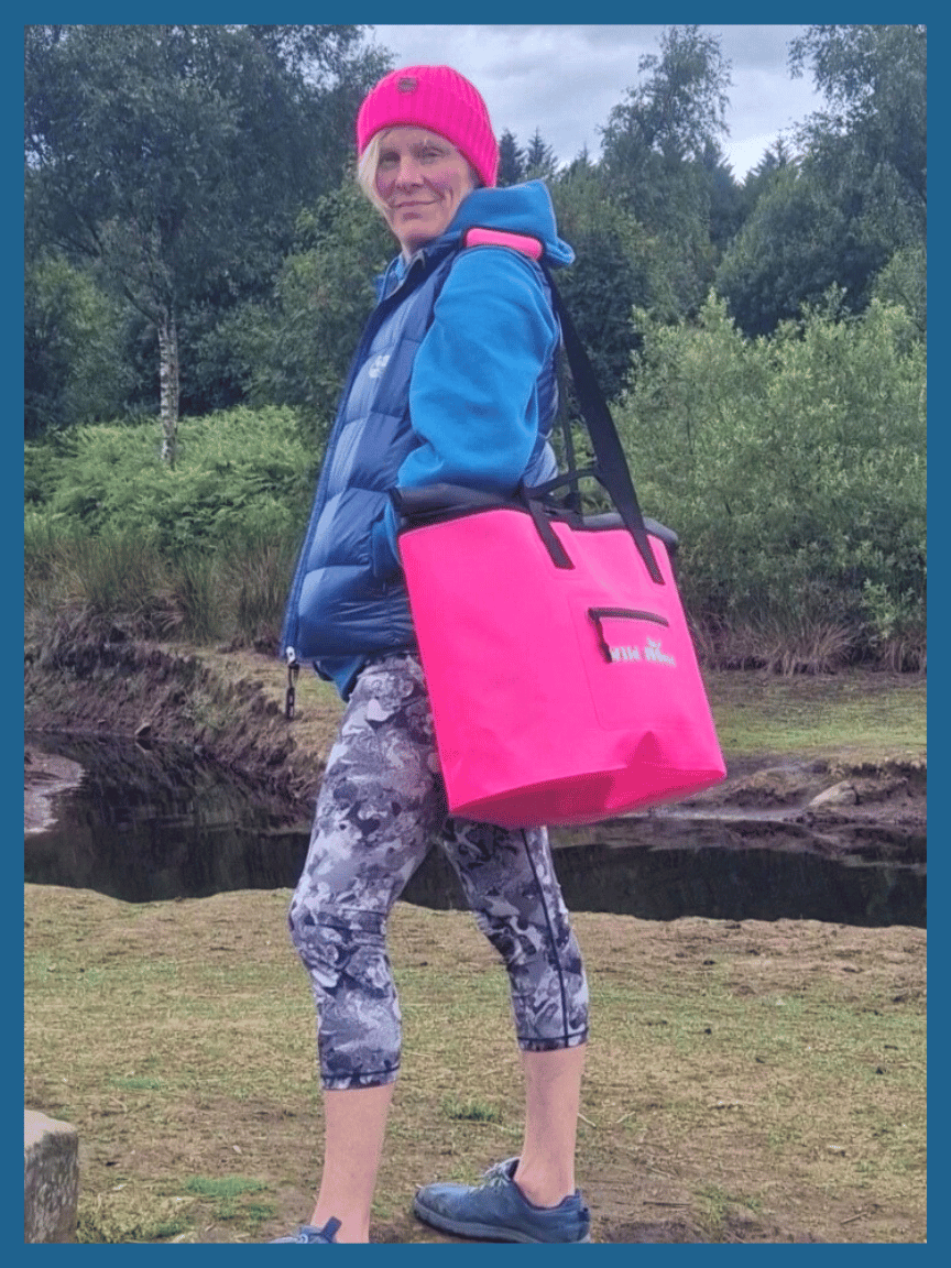 A Wild Swim Hiker Standing with a Bright Pink Wild Moose Waterproof Swim Bag wearing a pink beanie.