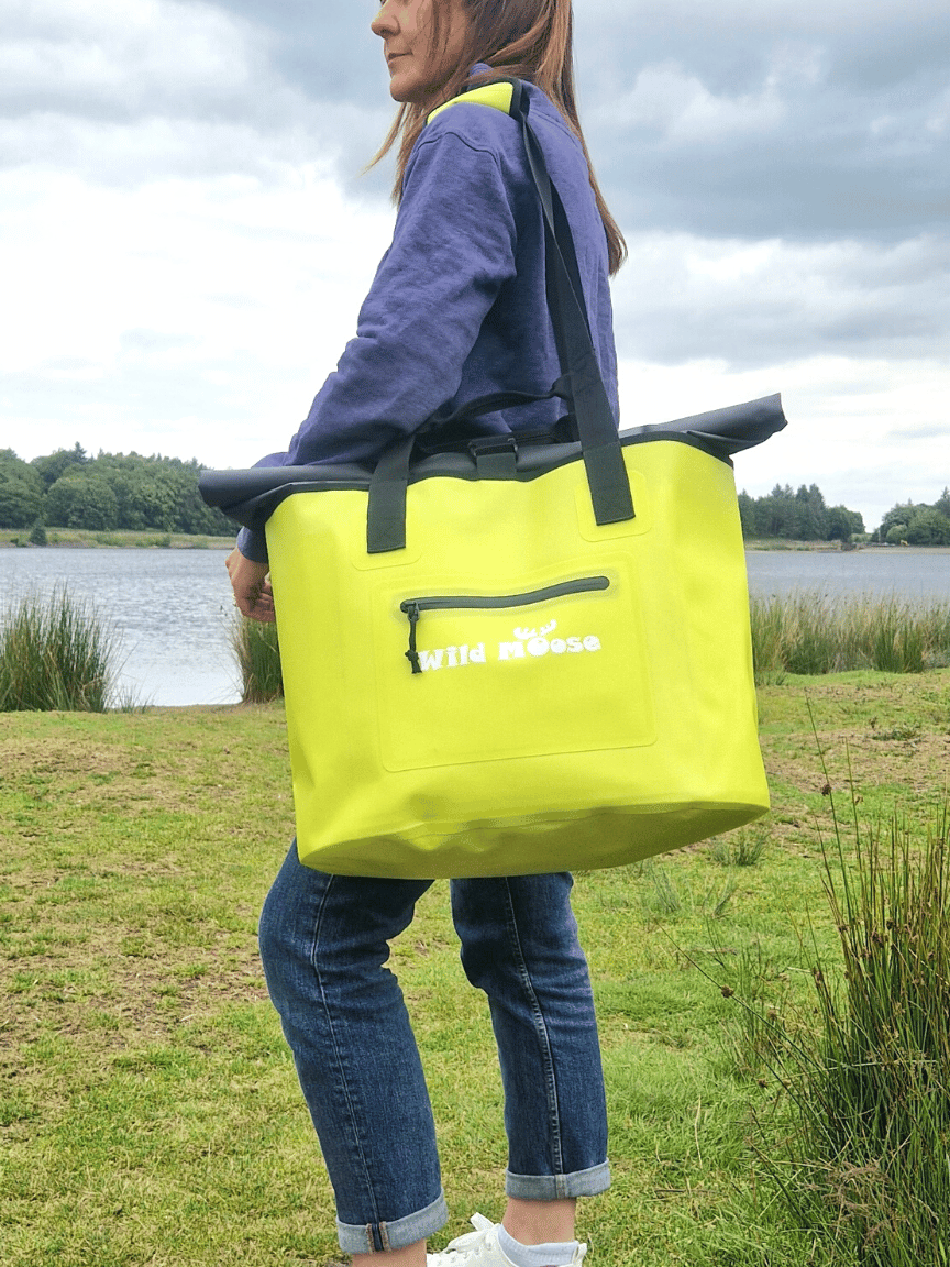 A Woman Standing by A Lake Wild Swimming Spot with a Wild Moose Yellow Waterproof Big Bag on her shoulder. Ideal for Wild Swimming.