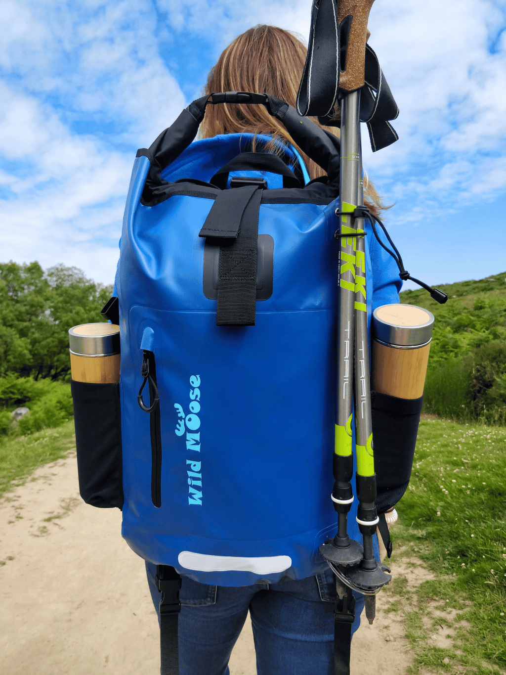 Hiker wearing a blue waterproof backpack with some walking poles in it. 