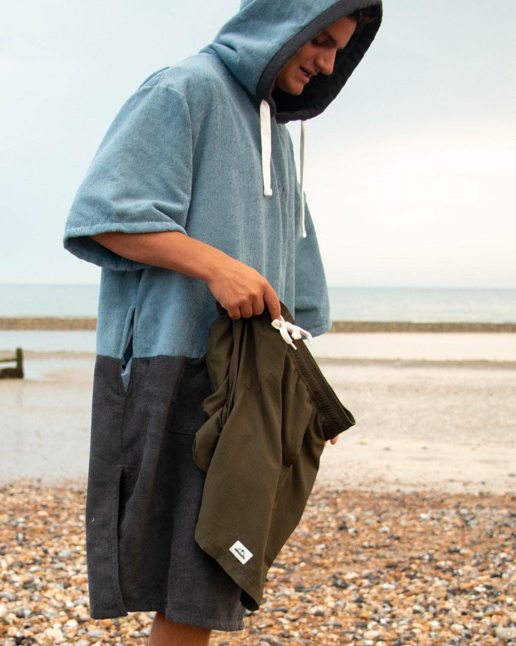 Man wears a Vivida Original Poncho Towel Changing Robe - Mineral Blue / Anthracite Grey