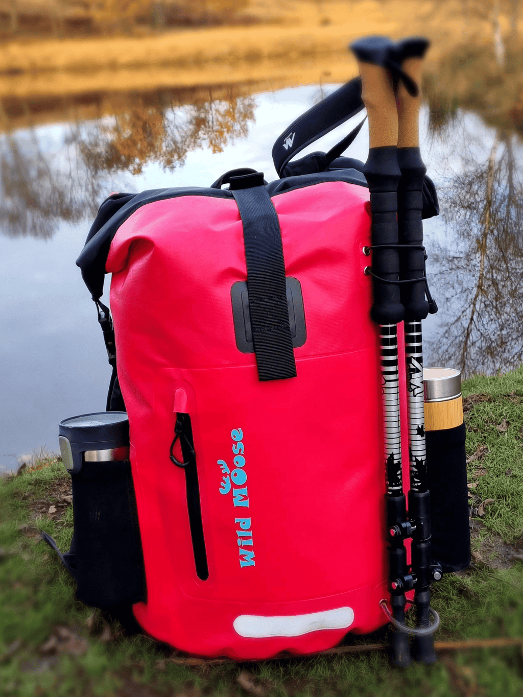 Bright pink waterproof 45L backpack by Wild Moose by a cold water swimming lake.