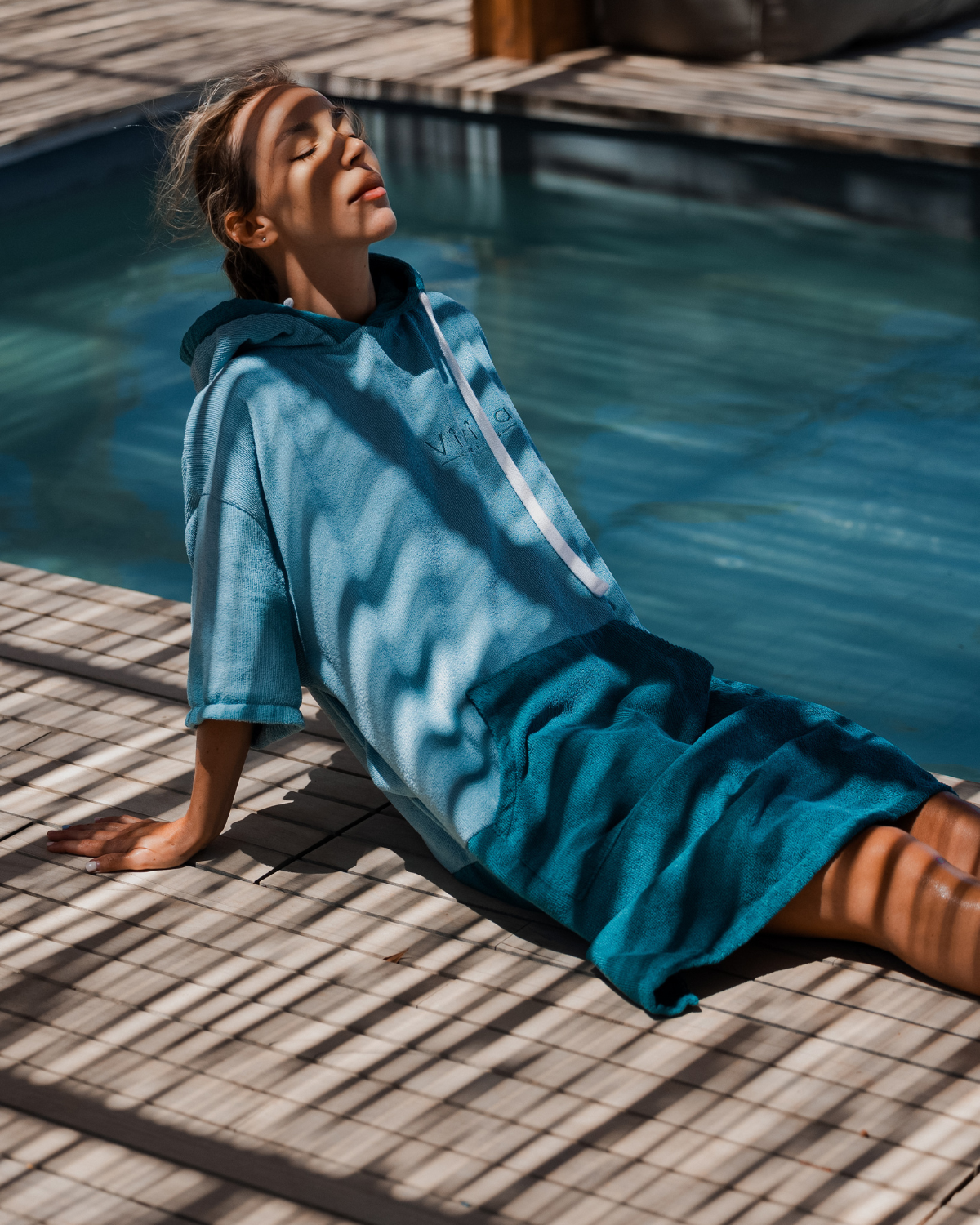 Woman wears a Vivida Original Adult Poncho Towel Changing Robe - Turquoise Teal / Pacific Teal. Sticker reads Women's Health Best Towelling Changing Robe