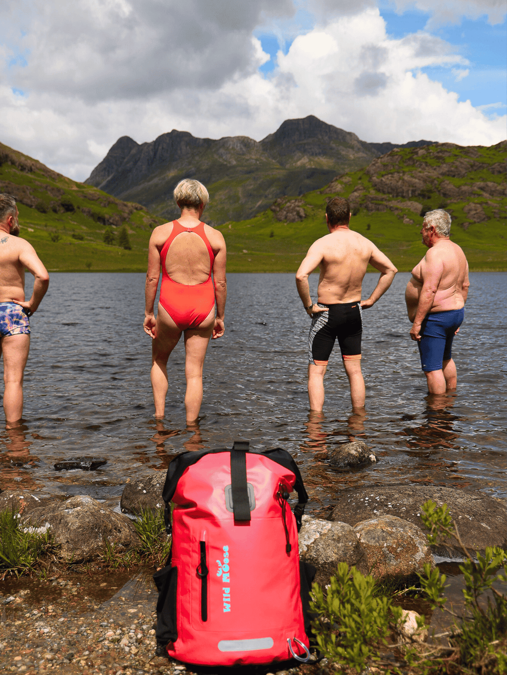 Group of Wild Swimmers in a lake swim spot with a pink waterproof swim bag in the foreground.