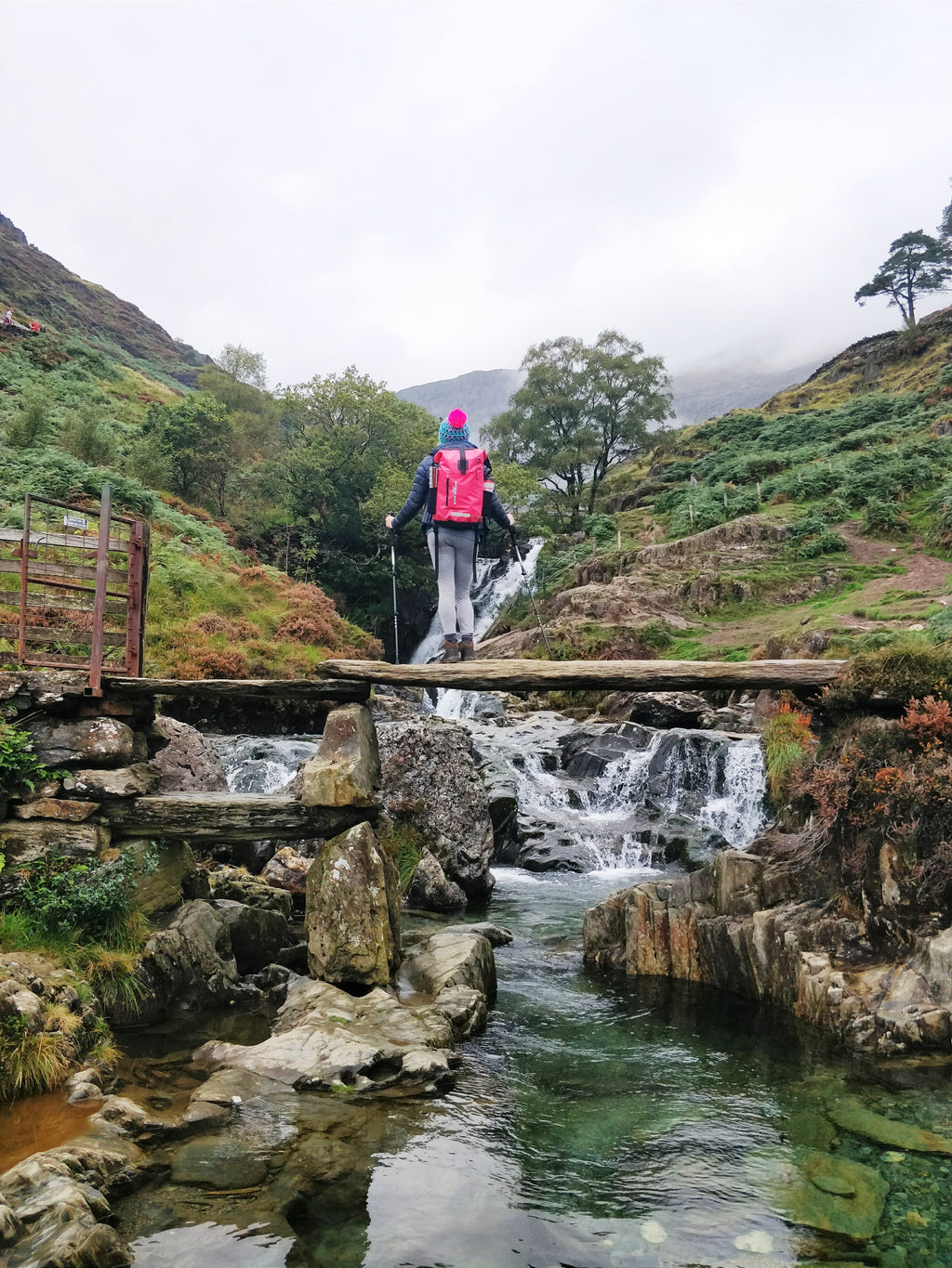 Wild Swimmer wearing bright pink waterproof swim backpack by Wild Moose, by waterfall and Blue Pools on the Watkins Path Snowdonia.
