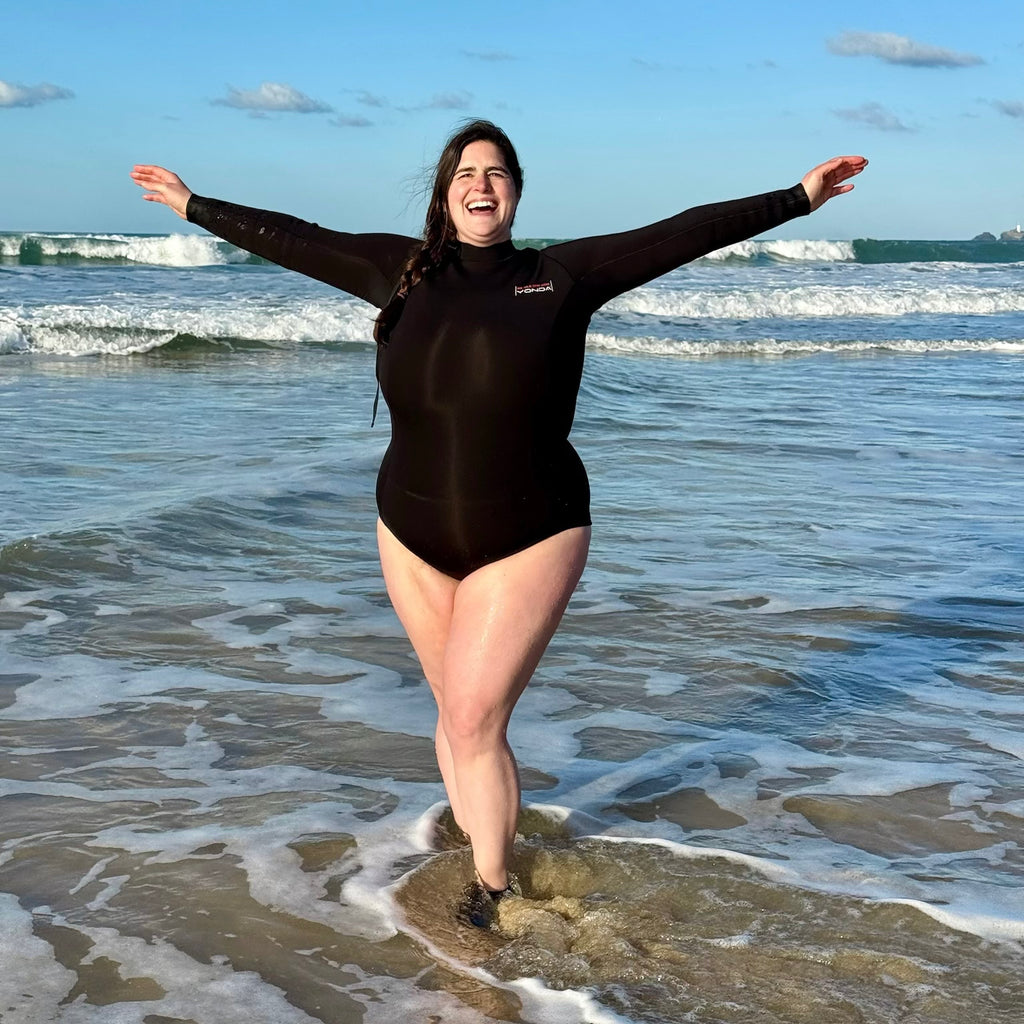 A Woman Plus Size Sea Swimmer in a black longsleeve swimsuit in the sea with her arms up, ideal for Cold Water Dipping.